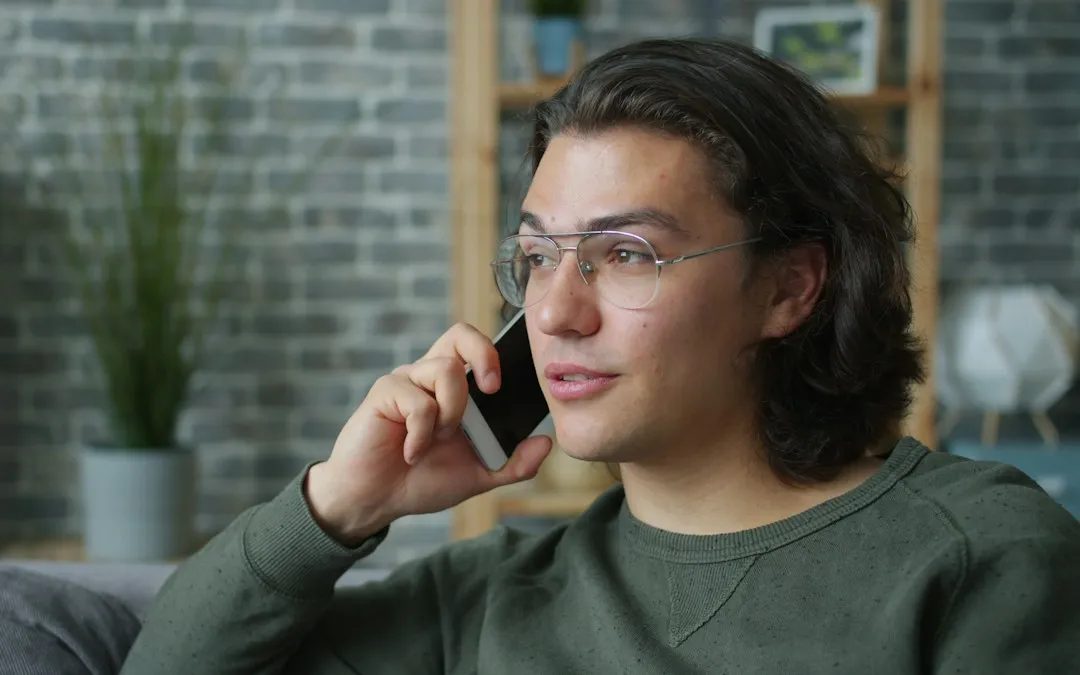 A man in glasses at home, listening on a phone call.