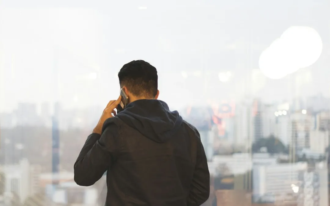 A man seen from behind at a window, on a phone call.